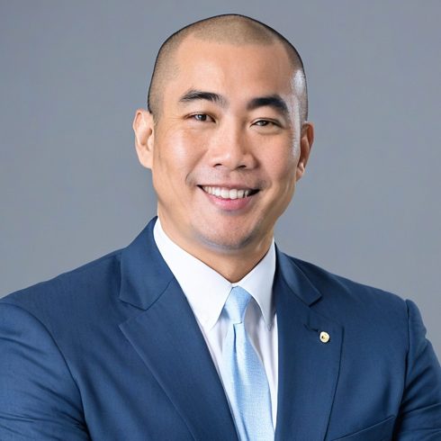 A person in a blue suit and light blue tie smiling with arms crossed against a gray background.